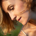 The picture shows a portrait in profile, taken in warm sunlight that falls on the skin and creates golden reflections in the light brown hair. The subject can be seen looking slightly downwards with a gentle smile, with fine details such as the delicately painted lips and naturally curved eyebrows emphasised by the soft light.