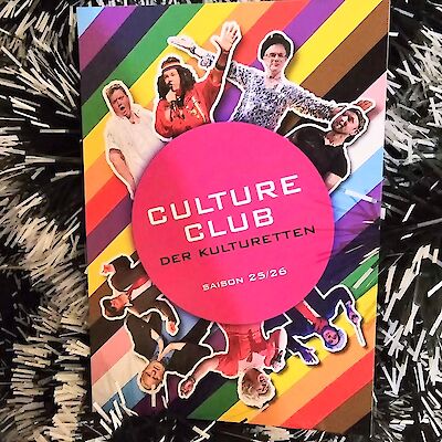 Das Bild zeigt ein buntes Werbeplakat für den Culture Club der Kultur(r)etten mit einem großen pinken Kreis in der Mitte, auf dem "CULTURE CLUB DER KULTUR(R)ETTEN SAISON 25/26" steht. Um den Kreis herum sind auf einem regenbogenfarbenen Hintergrund verschiedene ausgeschnittene Fotos von Personen in theatralischen Posen und Kostümen arrangiert, die die Darsteller der LGBTQ-Show zeigen.
