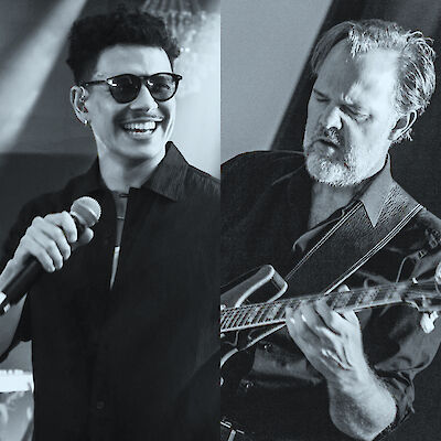 Ein schwarz-weißes Doppelbild zeigt auf der linken Seite einen lächelnden Mann mit Sonnenbrille und Mikrofon in der Hand, auf der rechten Seite einen älteren Mann mit Bart, der konzentriert E-Gitarre spielt. Beide Personen scheinen bei einem Live-Musikauftritt zu sein.