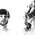 Ein schwarz-weißes Künstlerportrait zeigt zwei Personen vor weißem Hintergrund: links einen Mann mit kurzen Haaren und Dreitagebart, der ruhig in die Kamera blickt. Rechts ist eine Person zu sehen, deren langes, lockiges Haar dynamisch nach oben gewirbelt ist und das Gesicht verdeckt.